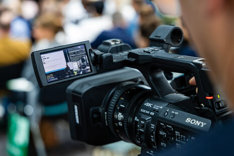 Eine Filmkamera, welche auf die Teilnehmer gerichtet ist.