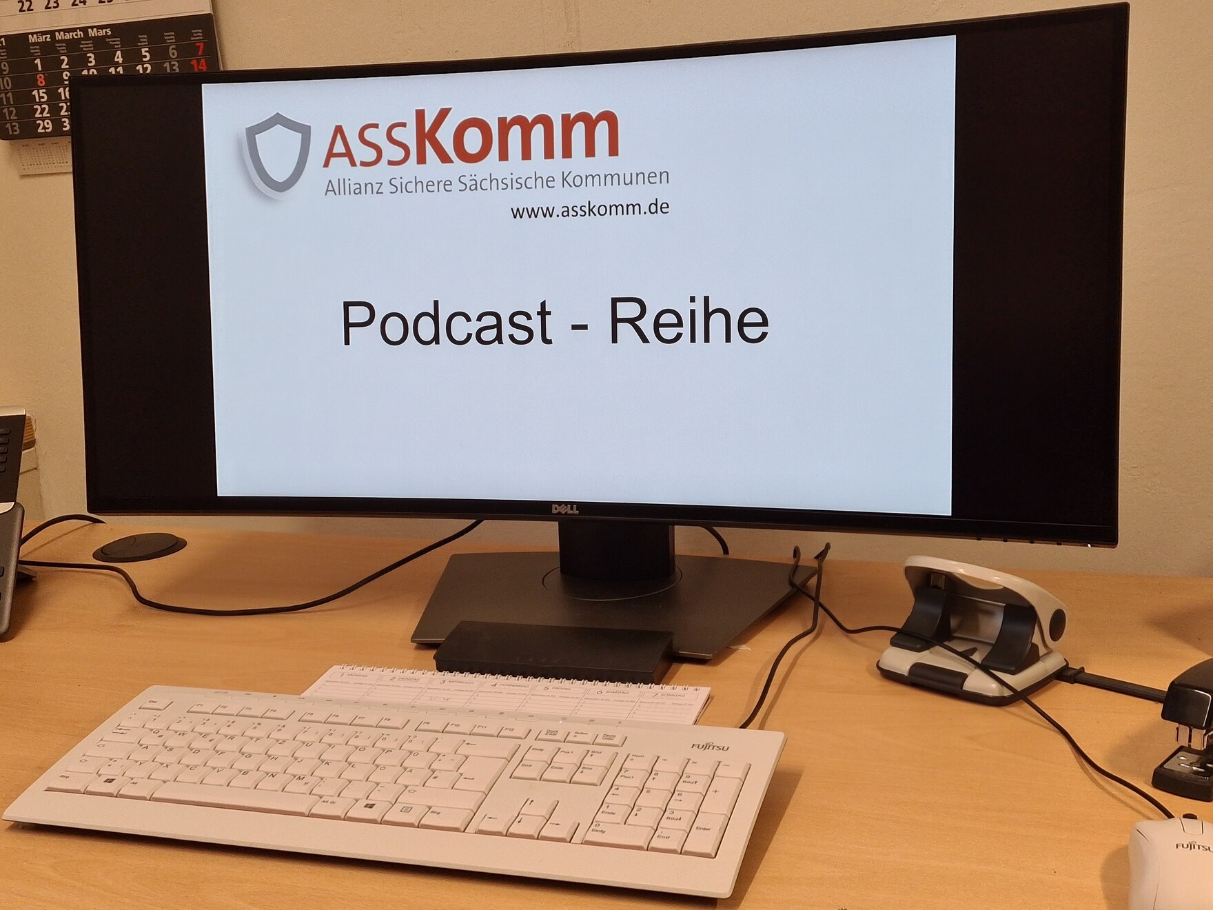 Ein Bildschirm mit der Aufschrift ASSKomm und Podcast-Reihe, davor eine Tastatur.