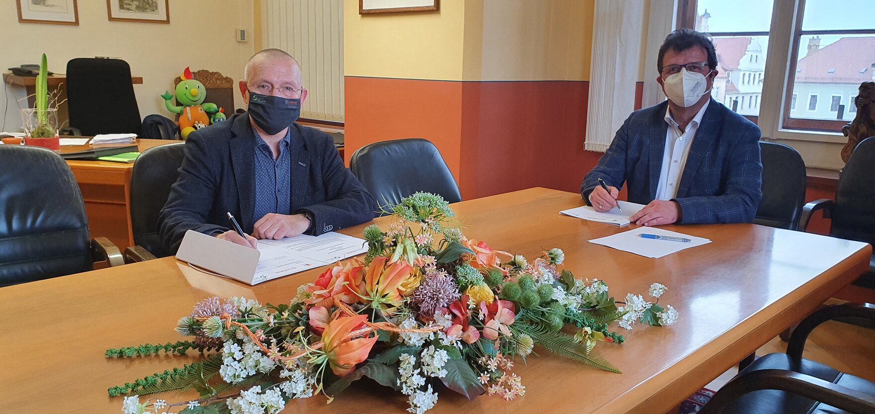 Der Bürgermeister der Stadt Oschatz und der Vertreter des Landespräventionsrates sitzen am Tisch und unterzeichnen jeweils die Kooperationsvereinbarung. Auf dem Tisch liegt ein Blumengesteck.