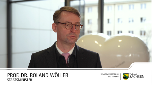 Staatsminister Prof. Dr. Roland Wöller steht im Sächsischen Staatsministerium und gibt ein Interview. Im Hintergrund sieht man das Sächsische Staatsministerium für Wirtschaft und Arbeit.
