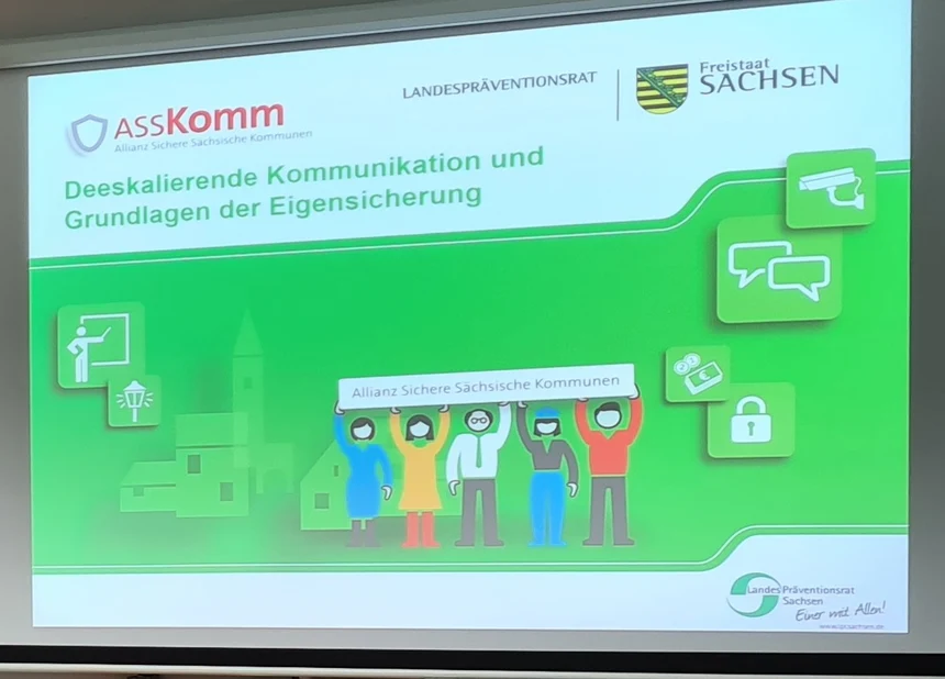 Präsentation des Vortragen von Torsten Kosuch zum Thema Gewalt und dessen Umgang beim Seminar Deeskalationstraining. Man sieht eine digitale Leinwand mit einer grünen Folie auf der das typische ASSKomm Logo zu sehen ist und dann das Thema des Vortrages