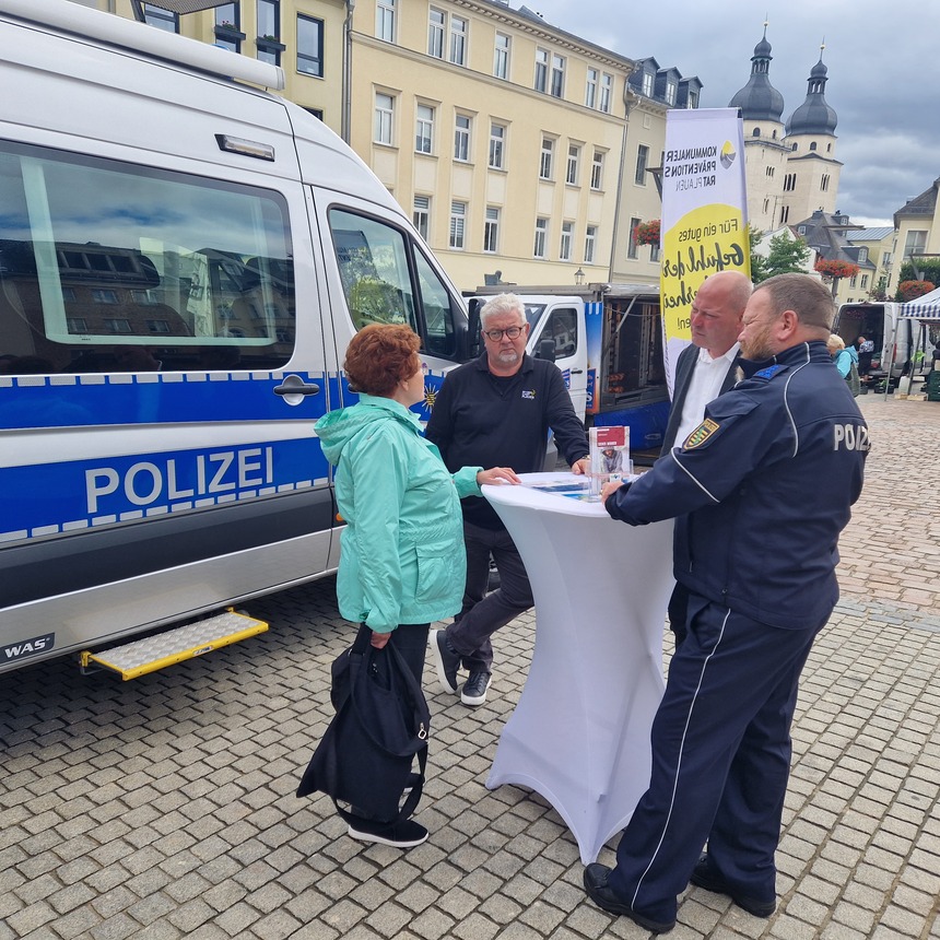 links ein Polizeibus, davor Mitglieder des Präventionsteams des KPR Plauens sowie eine Bürgerin 