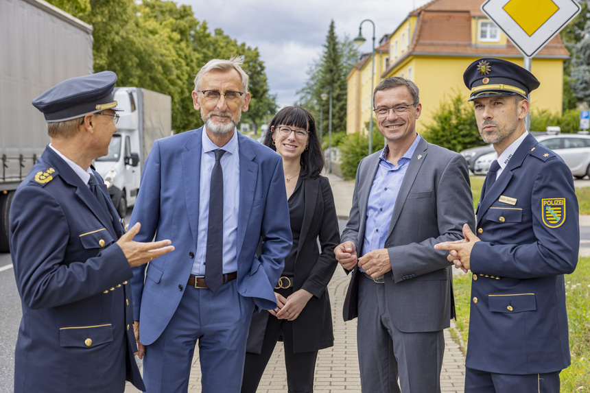 Fünf Personen stehen auf dem Bürgersteig in Wilsdruff. Im Hintergrund sieht man den Rückstau an einer Ampel.