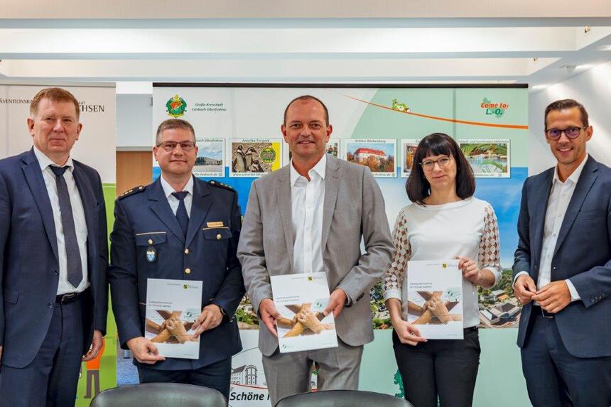 Fünf Personen stehen vor einem Bild von Limbach-Oberfrohna und drei halten eine Mappe in der Hand.