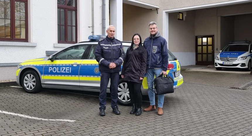Drei Personen stehen vor einem Streifenwagen.