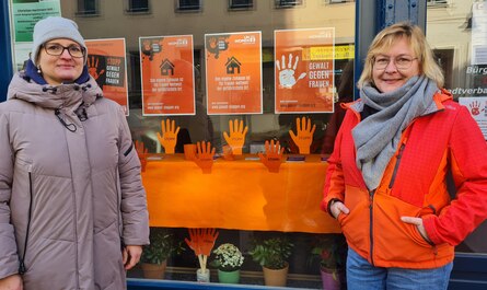 Zwei Frauen stehen vor einem Schaufenster, dass Informationen über Gewalt an Frauen enthält.