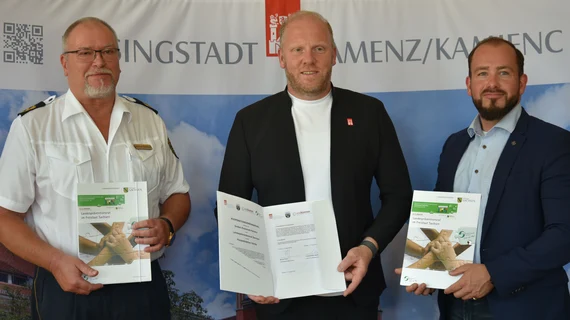 Drei Männer stehen und präsentieren die unterzeichnete Kooperationsvereinbarung.