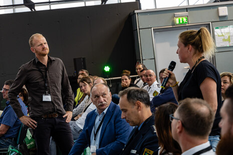 Der Referent spricht mit einer Teilnehmerin des Fachtages im Plenum.