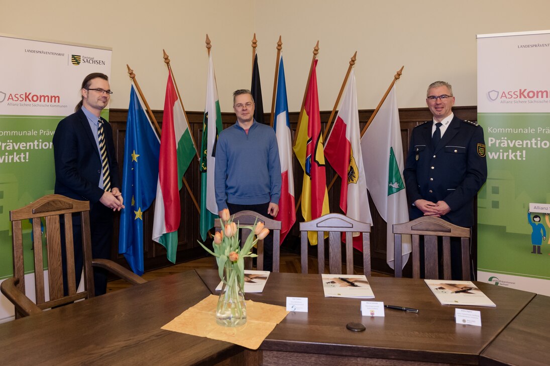 Sven Forkert, Geschäftsführer des Landespräventionsrates, Marcel Schmidt, Oberbürgermeister der Großen Kreisstadt Stollberg und André Regner, Leiter Polizeirevier Stollberg stehen hinter einem Tisch. Vor ihnen liegt die Kooperationsvereinbarung. 