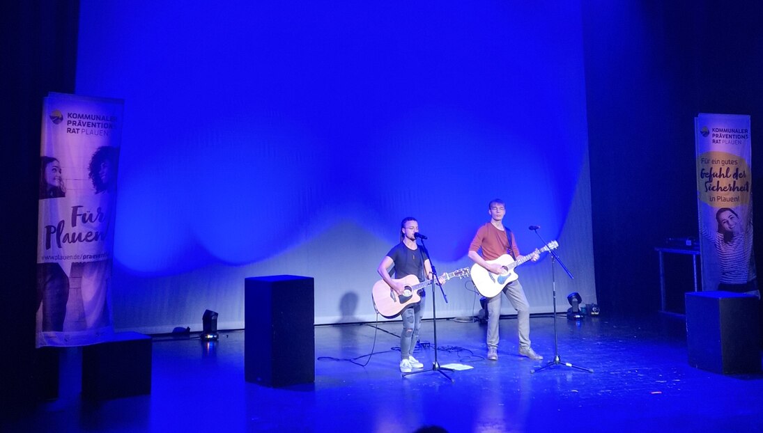 Zwei Jungs mit Gitarre stehen auf einer Bühne und singen.