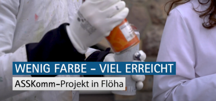 Auf dem Bild sieht man einen Menschen mit weißem Kittel, der eine Spray-Flasche in der Hand hält. Darunter steht der Schriftzug: Wenig Farbe Viel erreicht. ASSKomm Projekt in Flöha.