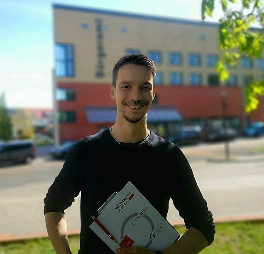 zeigt John Detzner im Portrait vor einem Gebäude 