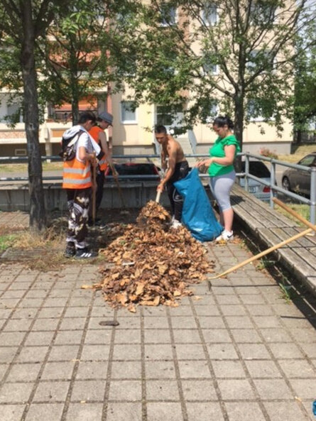 Jugendliche kehren den Boden rund um eine Sitzgruppe im Freien.