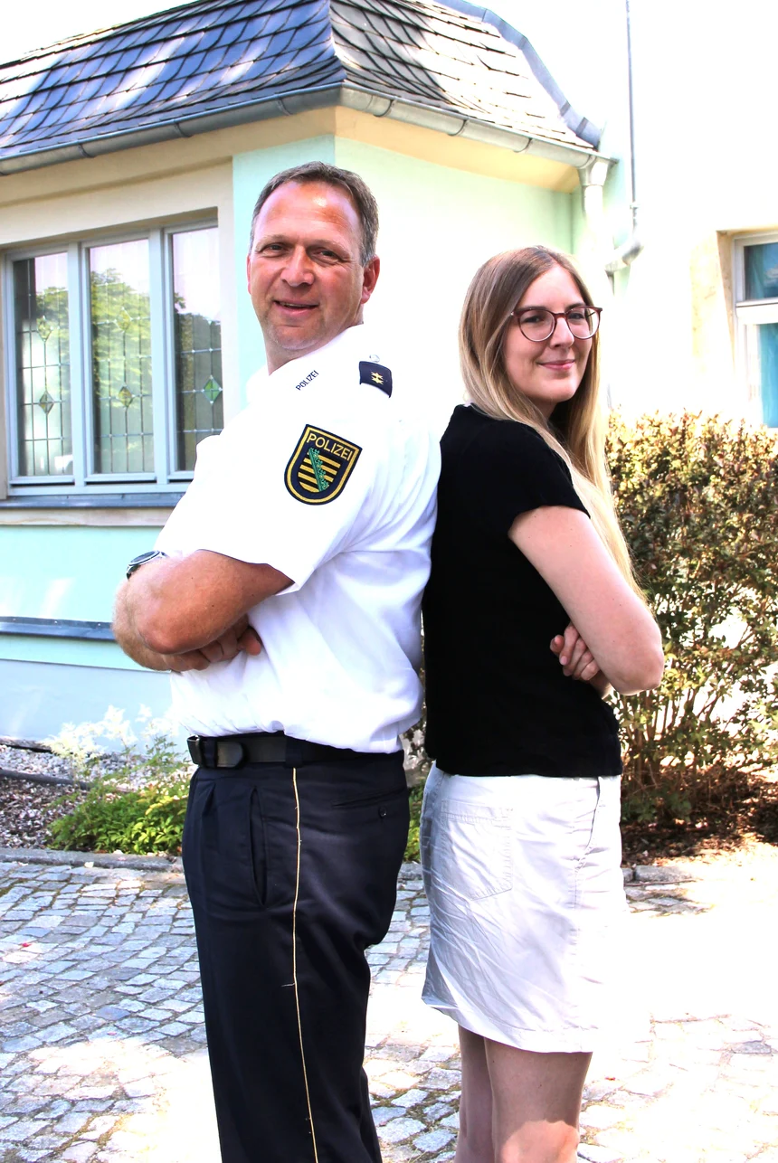 Der Mann in Uniform und die Frauen stehen mit dem Rücken aneinander und lächeln in die Kamera.