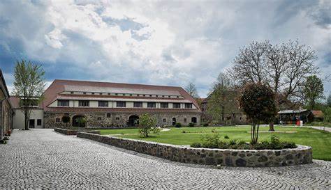 Das Haupthaus des Hotels Gut am See steht im Hintergrund an einer Rasenfläche und Bäumen.