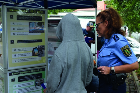 Man sieht eine Polizistin und eine weitere Person vor einem Plakat.