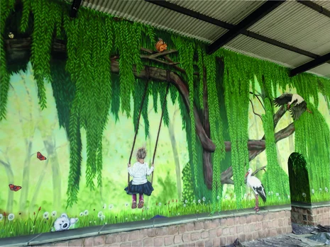 Man sieht Graffiti an einer Wand. Dieses zeigt ein Kind auf einer Schaukel, einen Baum und Vögel.