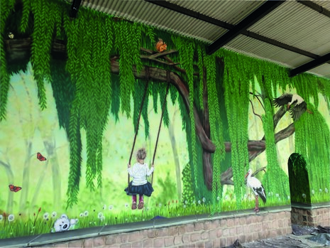 Man sieht Graffiti an einer Wand. Dieses zeigt ein Kind auf einer Schaukel, einen Baum und Vögel.