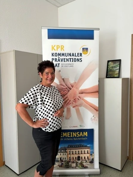 Eine Frau steht in einem Raum vor einem Aufsteller des Kommunalen Präventionsrates der Stadt.