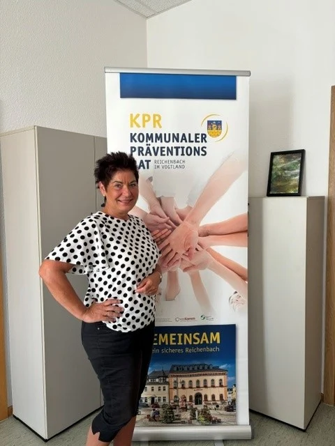 Eine Frau steht in einem Raum vor einem Aufsteller des Kommunalen Präventionsrates der Stadt.