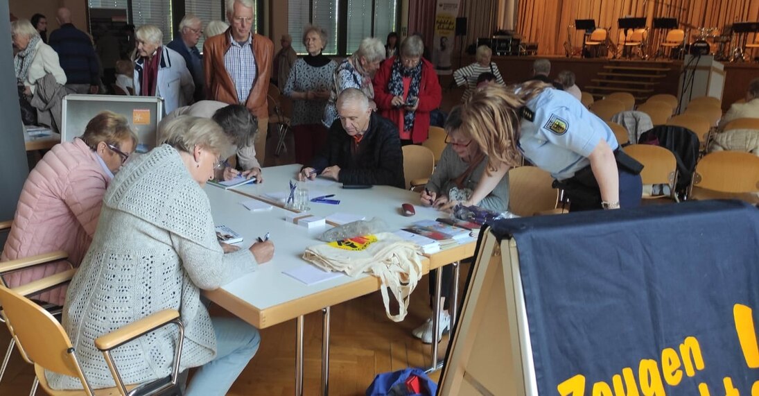 Senioren sitzen an einem Informationsstand und werden von einer Bundespolizistin betreut.