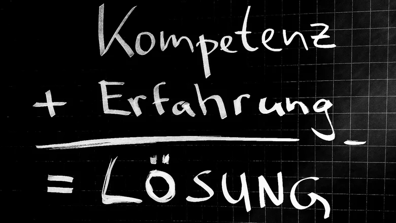 Schwarze Tafel mit der Schrift Kompetenz + Erfahrung = Lösung