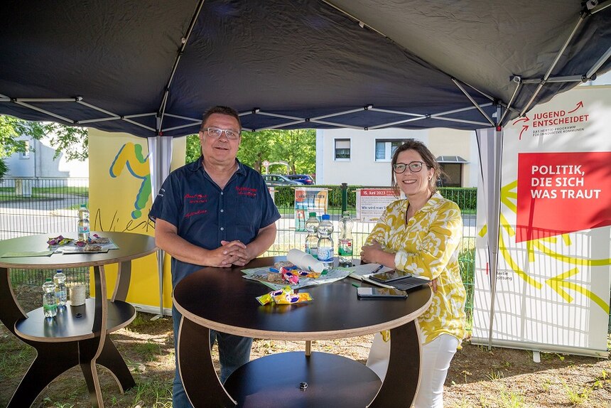 zeigt Martin Giese und Oberbürgermeisterin Kathrin Uhlemann an einem Tisch unter einem Pavillon 