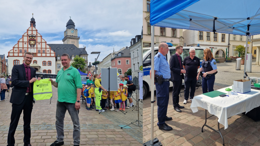 auf der Linken Seite der Bürgermeister Tobias Kämpf und eine weitere Person halten einen gelben Rucksack mit der Aufschrift: Kommunaler Präventionsrat Plauen, hoch, im Hintergrund eine Schulklasse, rechts 4 Personen am Stand des KPR Plauen