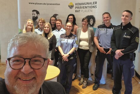 Auf dem Bild sieht man viele Personen vor einem Aufsteller des kommunalen Präventionsrates. Ein Mann macht mit ihnen ein Selfie.