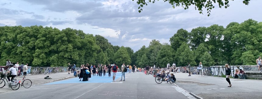 Die Sachsenbrücke in Leipzig ist dargestellt. Darauf laufen viele Personen. Es ist ein Hotspot der Partyszene in Leipzig. 