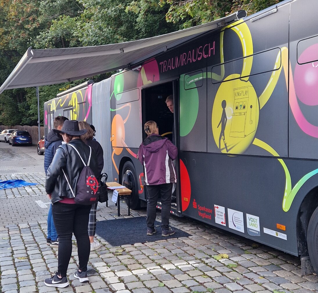 Der Suchtbus steht auf einem Platz und vier Menschen warten davor.