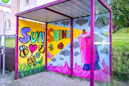 Buswartehäuschen mit Graffiti bemalt und dem Schriftzug "Sunshine", der aus einer Spraydose kommt.