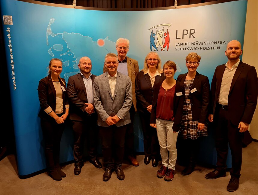 Acht Personen stehen vor einem Banner des LPR Schleswig-Holstein.