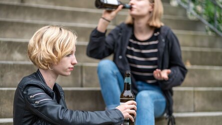 zeigt Symbolbild von zwei Personen sitzend auf einer Treppe mit Bierflaschen in der Hand