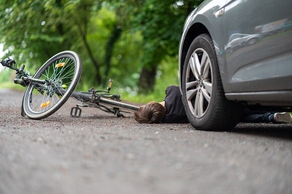 Ein Autounfall ist abgebildet. Ein Fahrradfahrer liegt am Boden vor einem Auto